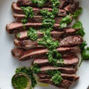 Sliced grilled steak on a plate with chimichurri sauce drizzled on top.