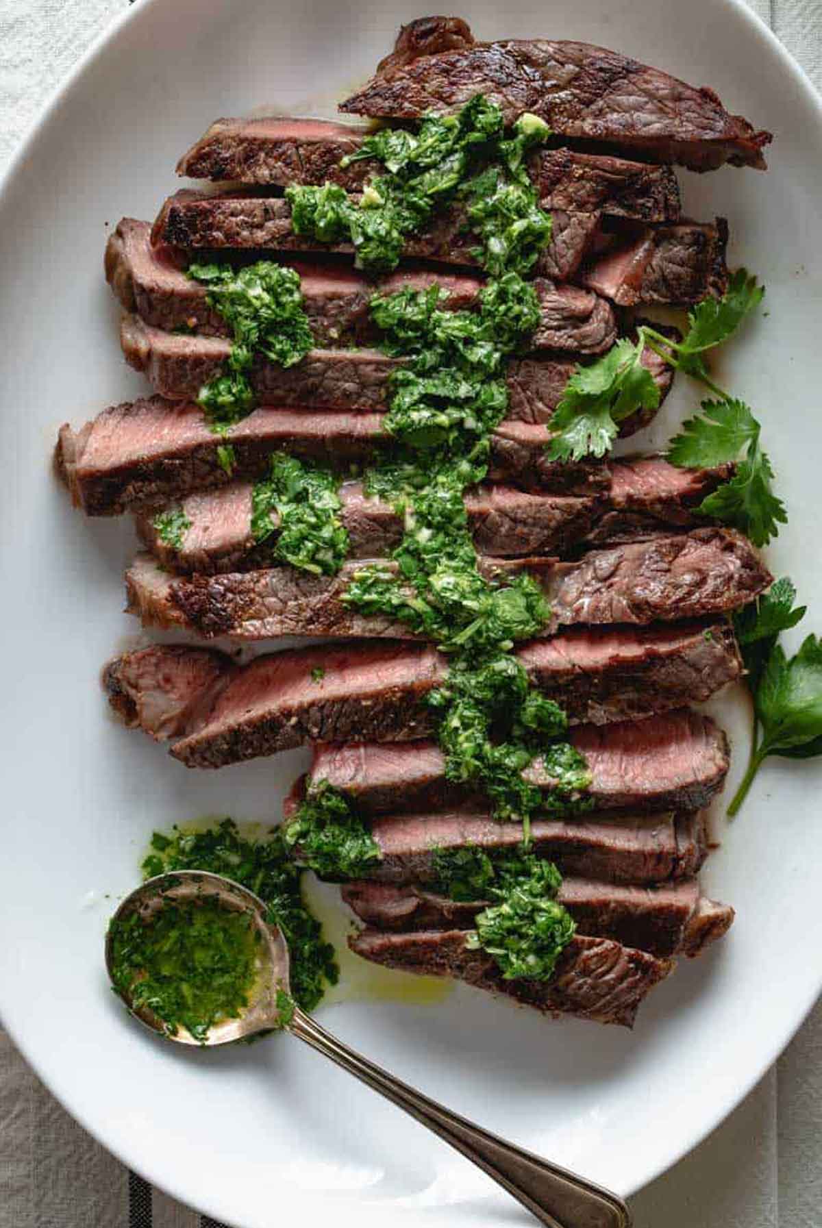 Sliced grilled steak on a plate with chimichurri sauce drizzled on top.