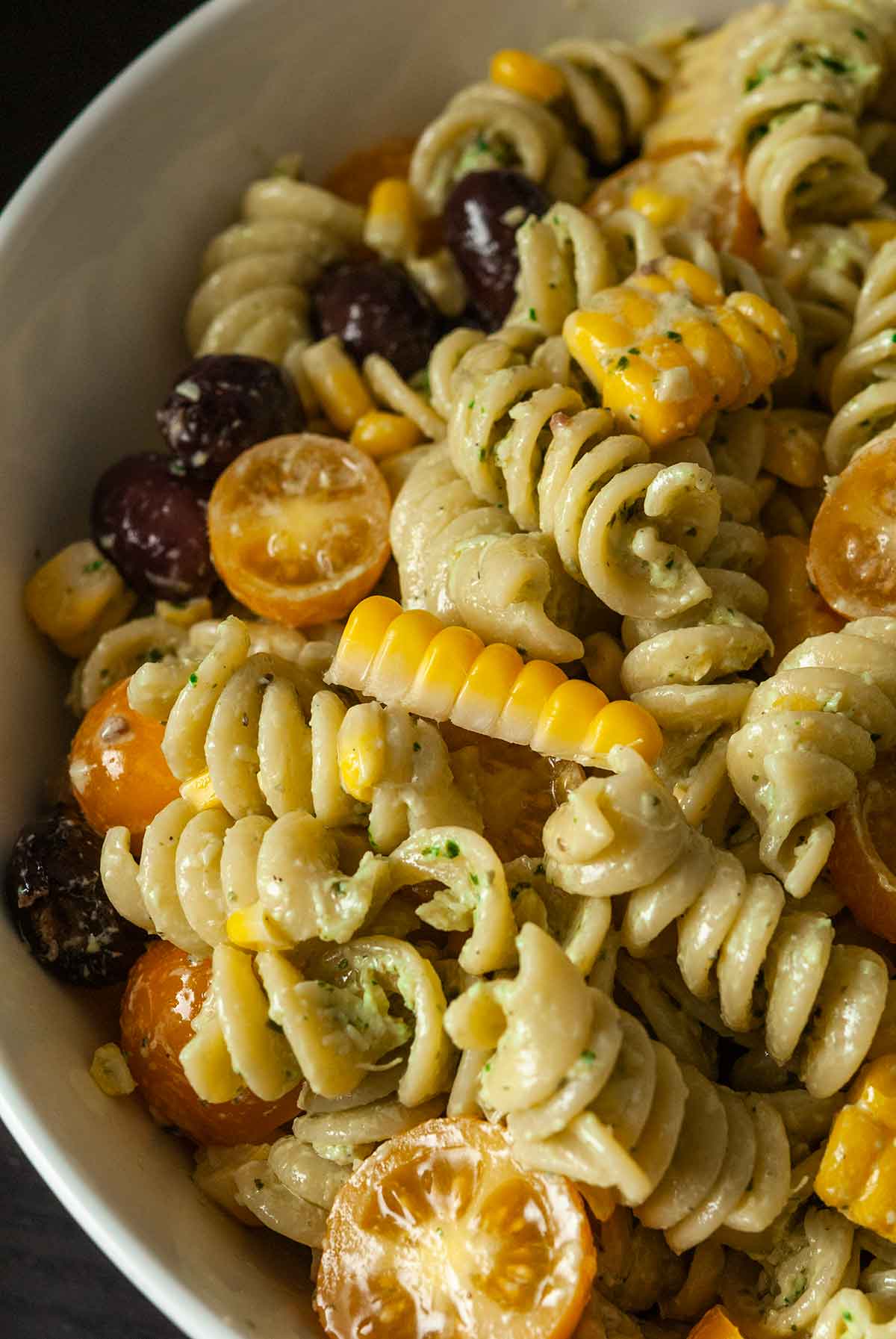 A bowl of pasta salad with fresh corn, tomatoes and olives.