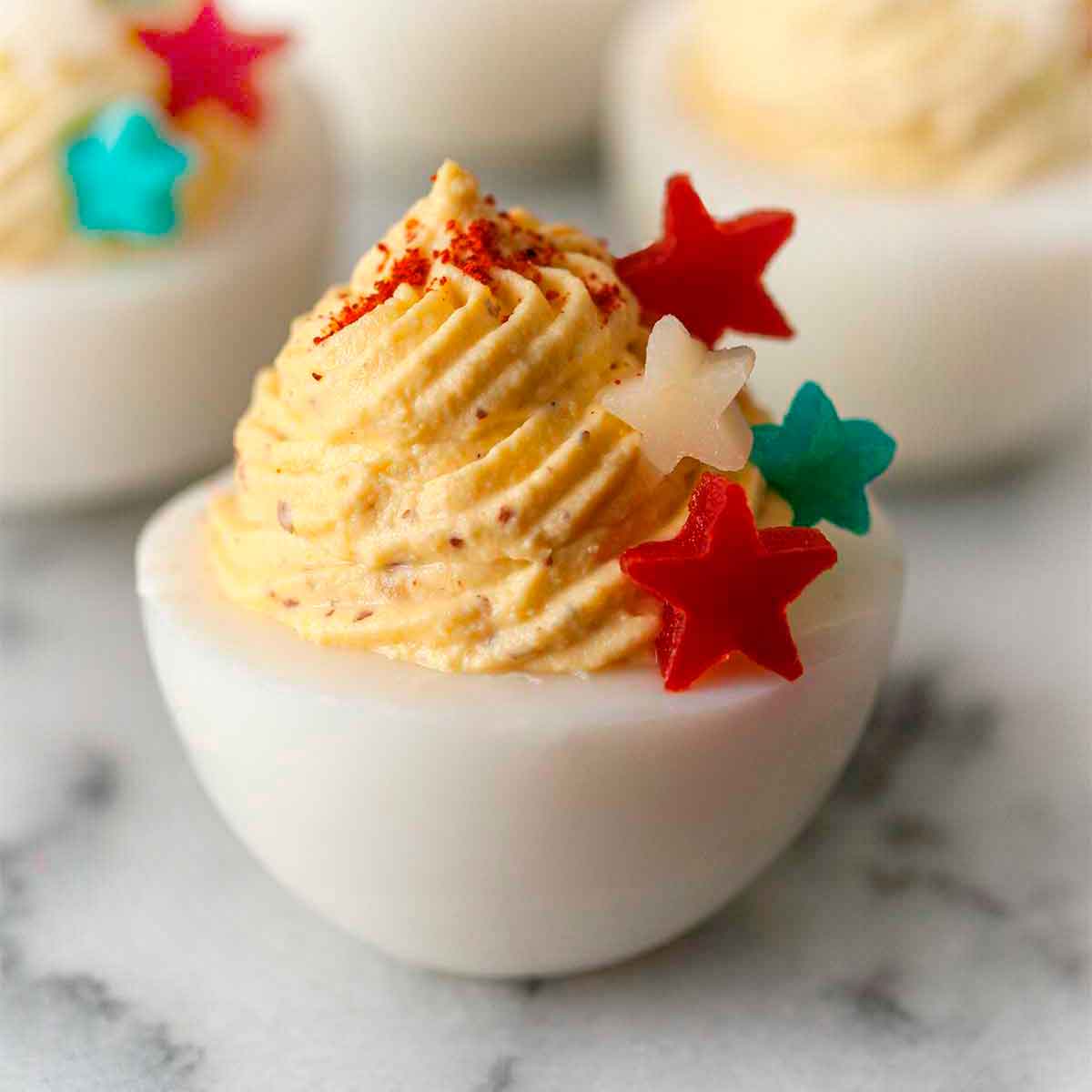 A deviled egg on marble, garnished with 4 stars made of red peppers and cheese that's both blue and white.