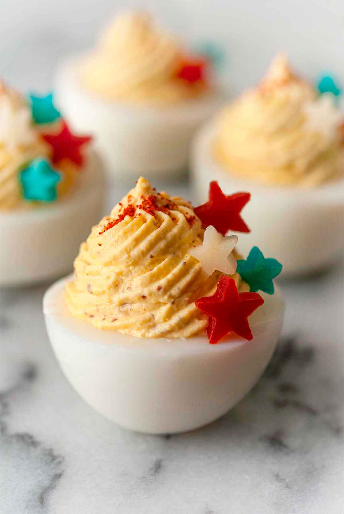 4 deviled eggs on marble, garnished with 4 stars made of red peppers and cheese that's both blue and white.