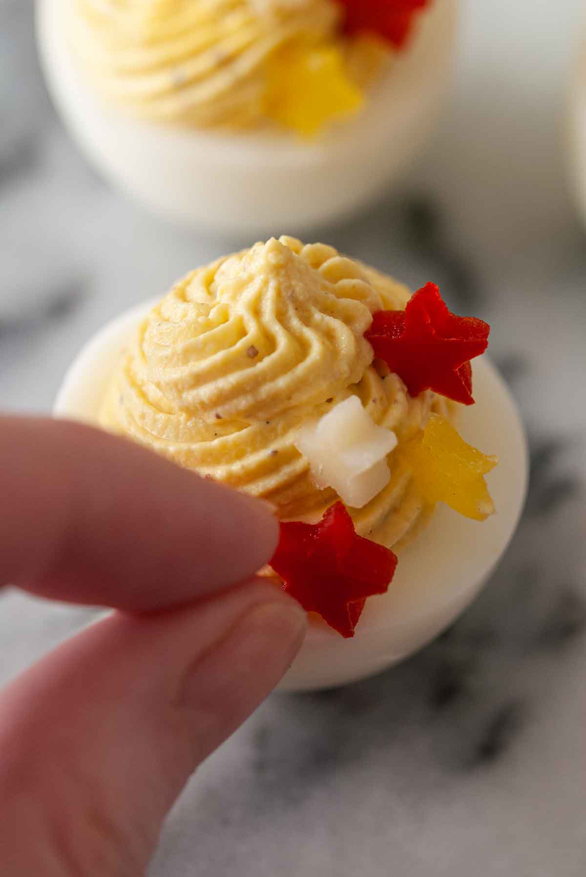 Fingers adding a pepper star garnish to a deviled egg.