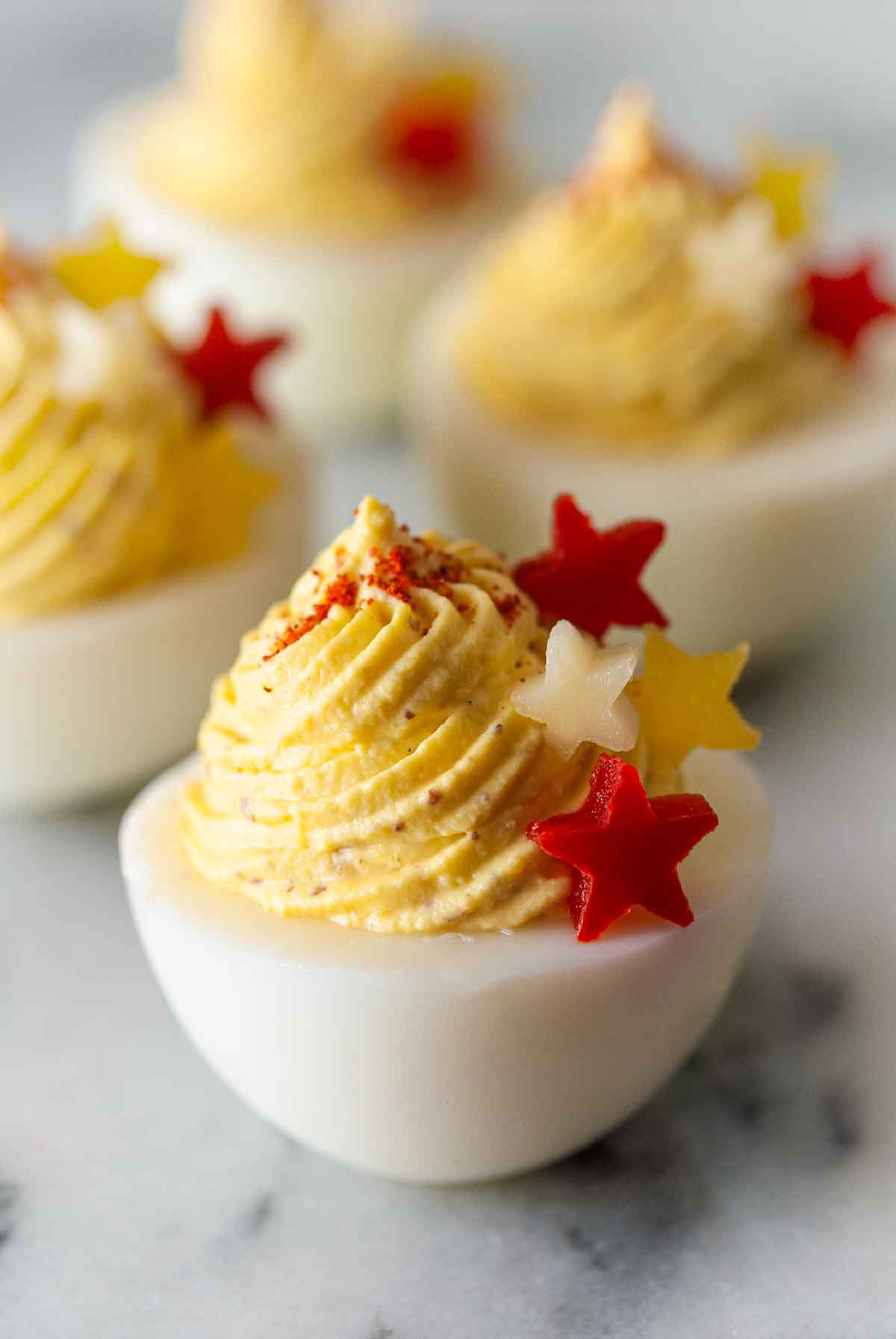 4 deviled eggs on marble, garnished with 4 stars made of red and yellow peppers and cheese.