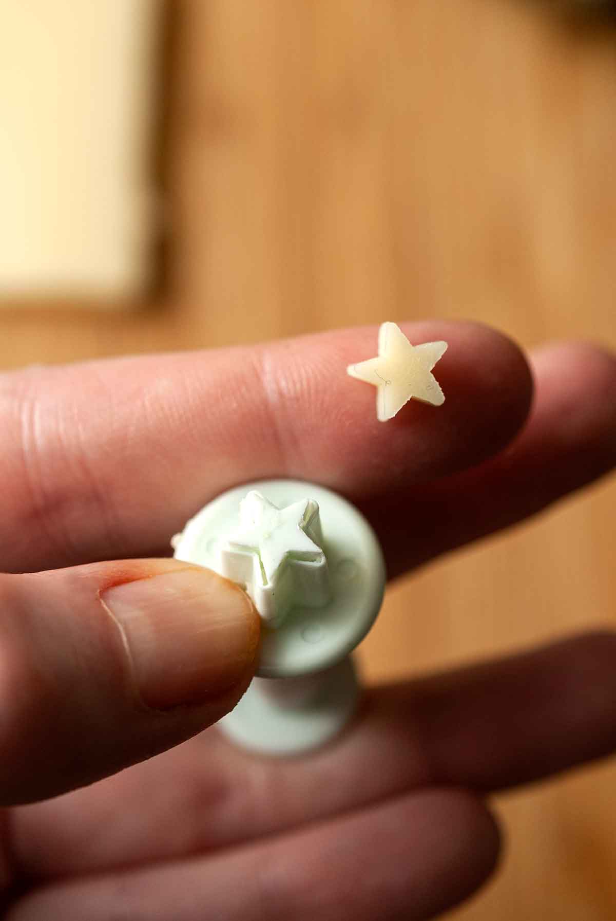 A hand holding a tiny star puncher with a small cheese star on the pointer finger.