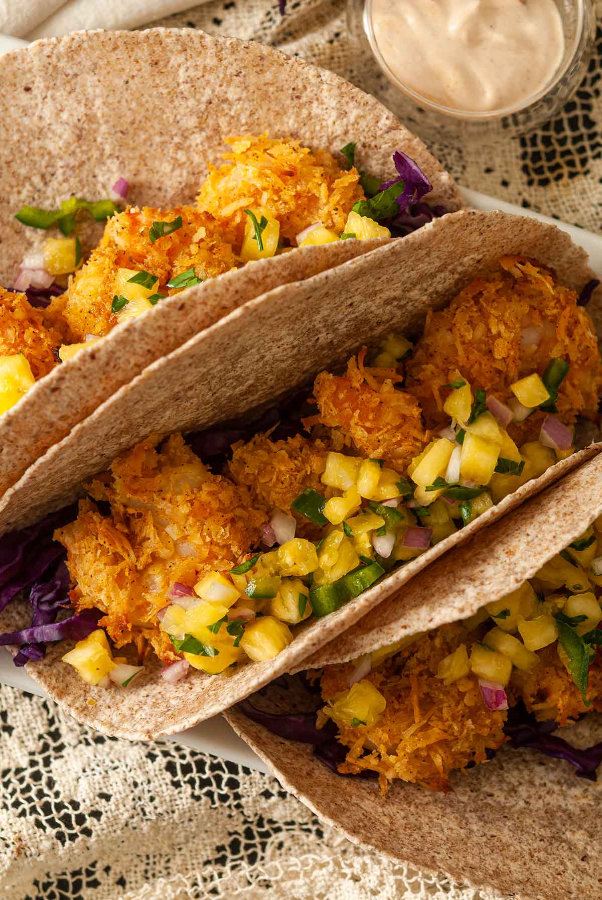 3 coconut shrimp tacos topped with pineapple jalapeño salsa on a table.