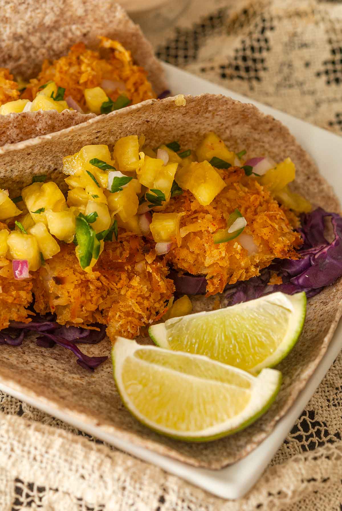 The shrimp and pineapple salsa in a taco beside 2 slices on lime on a plate.