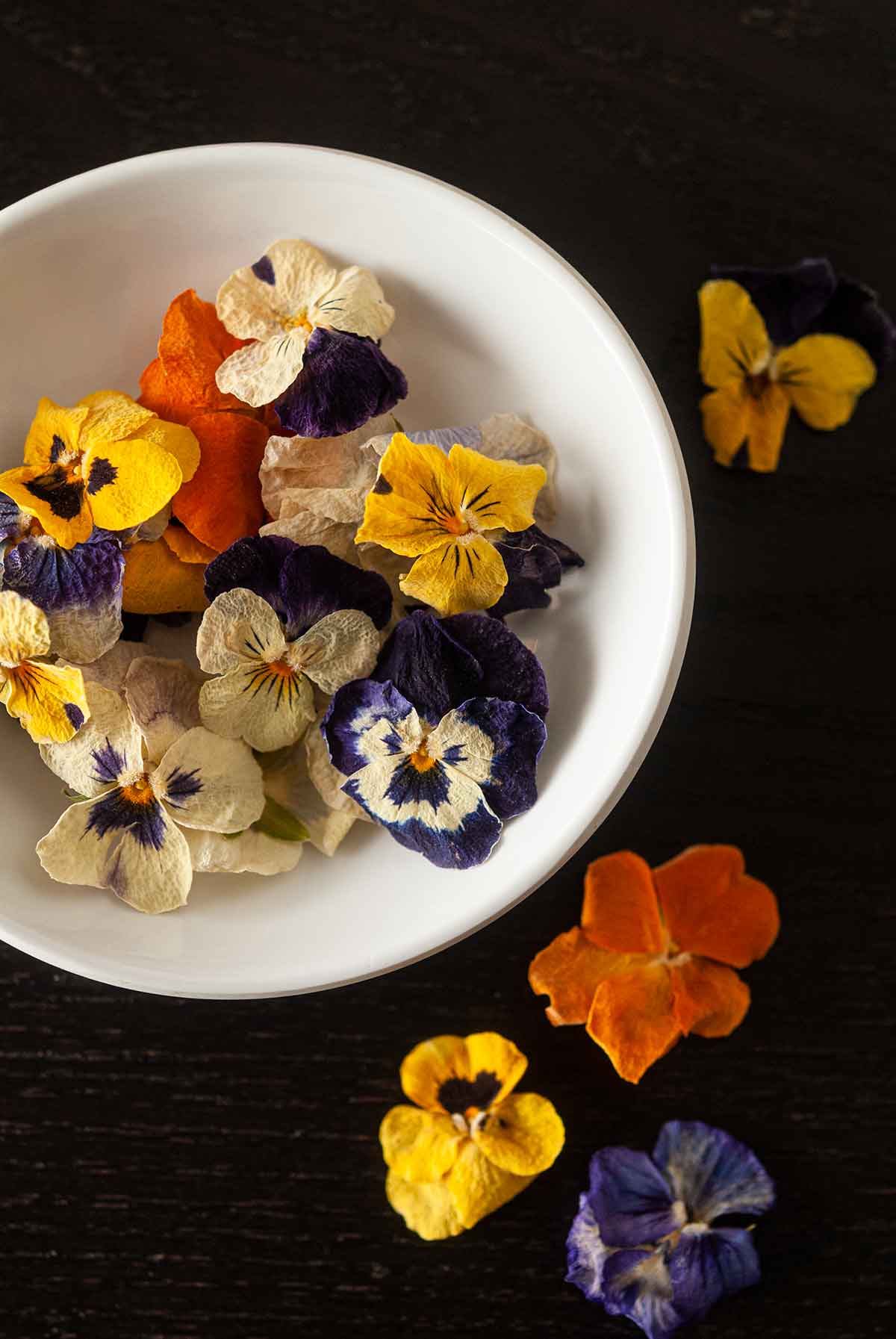 A bowl of small, dry pansies with a few flowers scattered around the bowl.