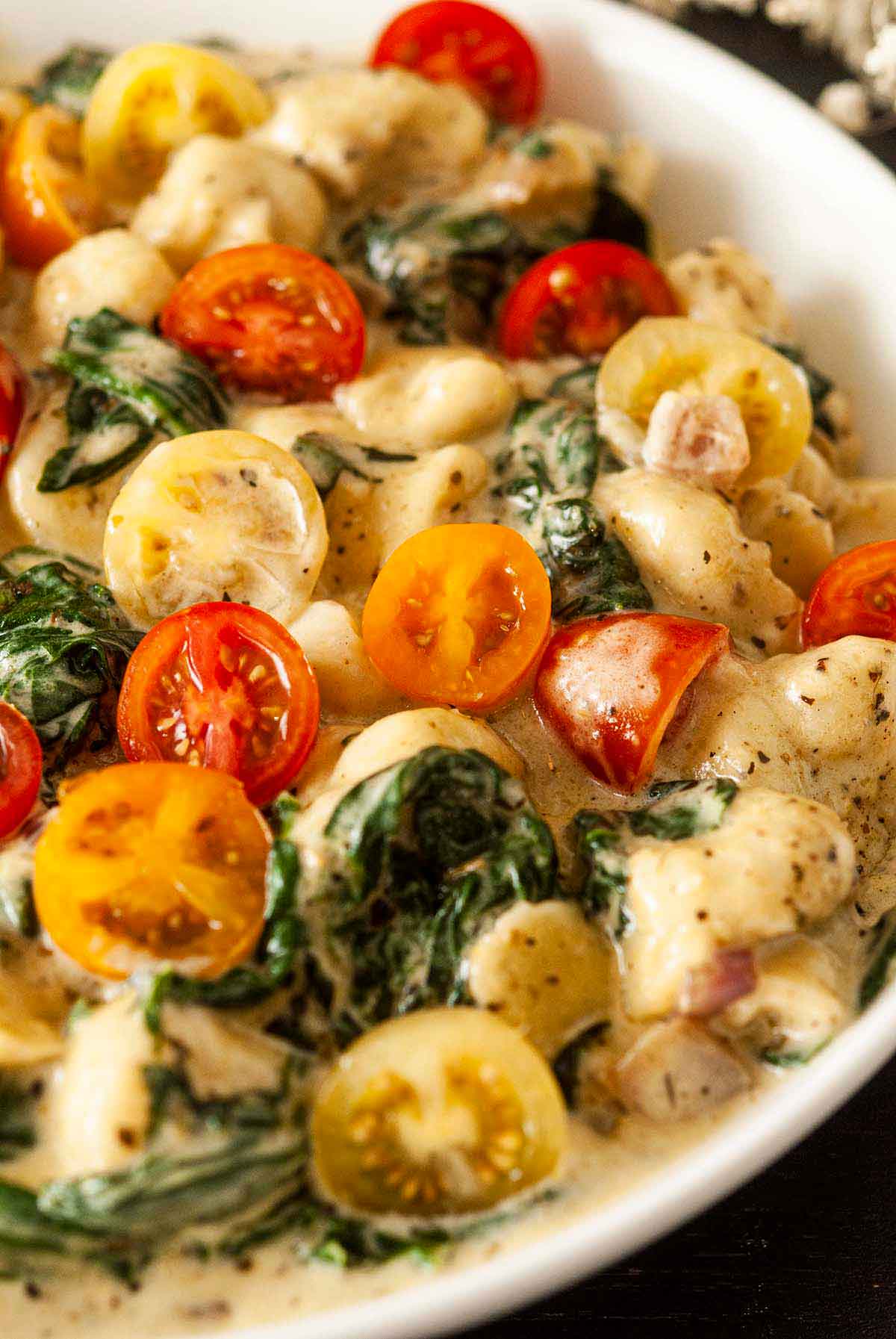 A bowl of colorful gnocchi with tomatoes and spinach in a bowl.