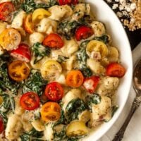 A bowl of colorful gnocchi with tomatoes and spinach in a bowl.