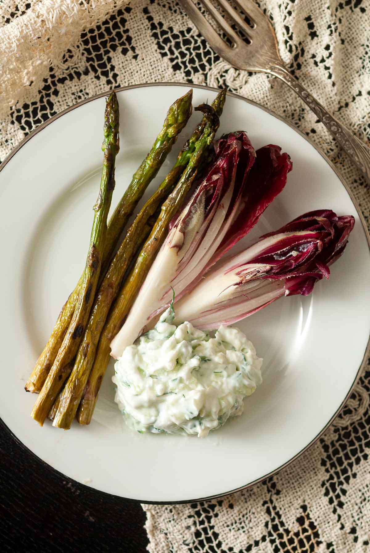 A plate with 2 sliced endive, 4 asparagus and a small pile of tzatziki.