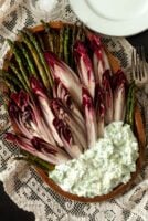 Endive and asparagus on a plate with a pile of tzatziki on a table cloth beside forks and plates.
