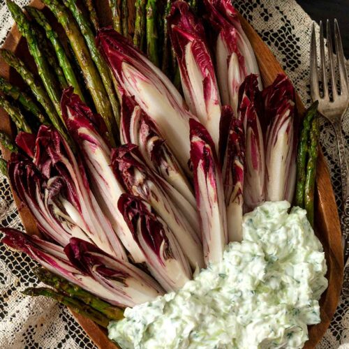 Endive and asparagus on a plate with a pile of tzatziki on a table cloth beside forks and plates.