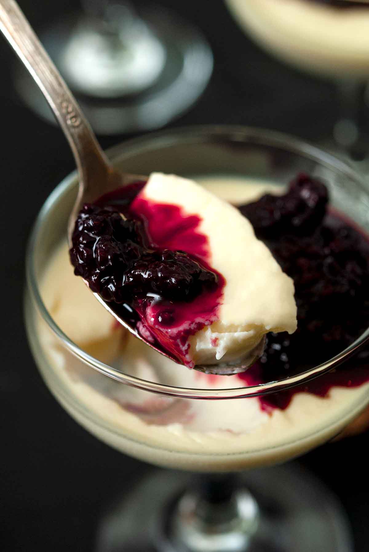 A spoon full of panna cotta and berry sauce over a glass of the dessert.