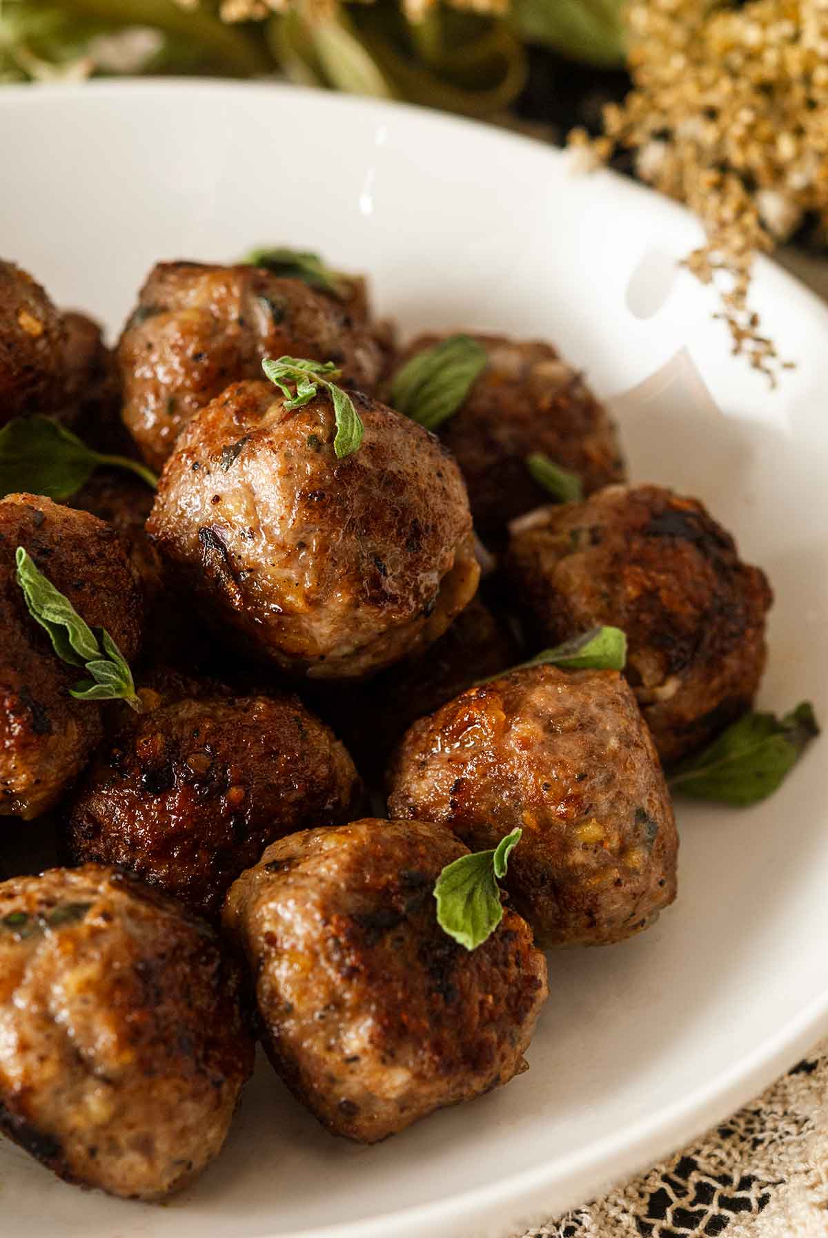 About 15 meatballs in a bowl (close shot), sprinkled with fresh oregano, surrounded by wispy flowers.