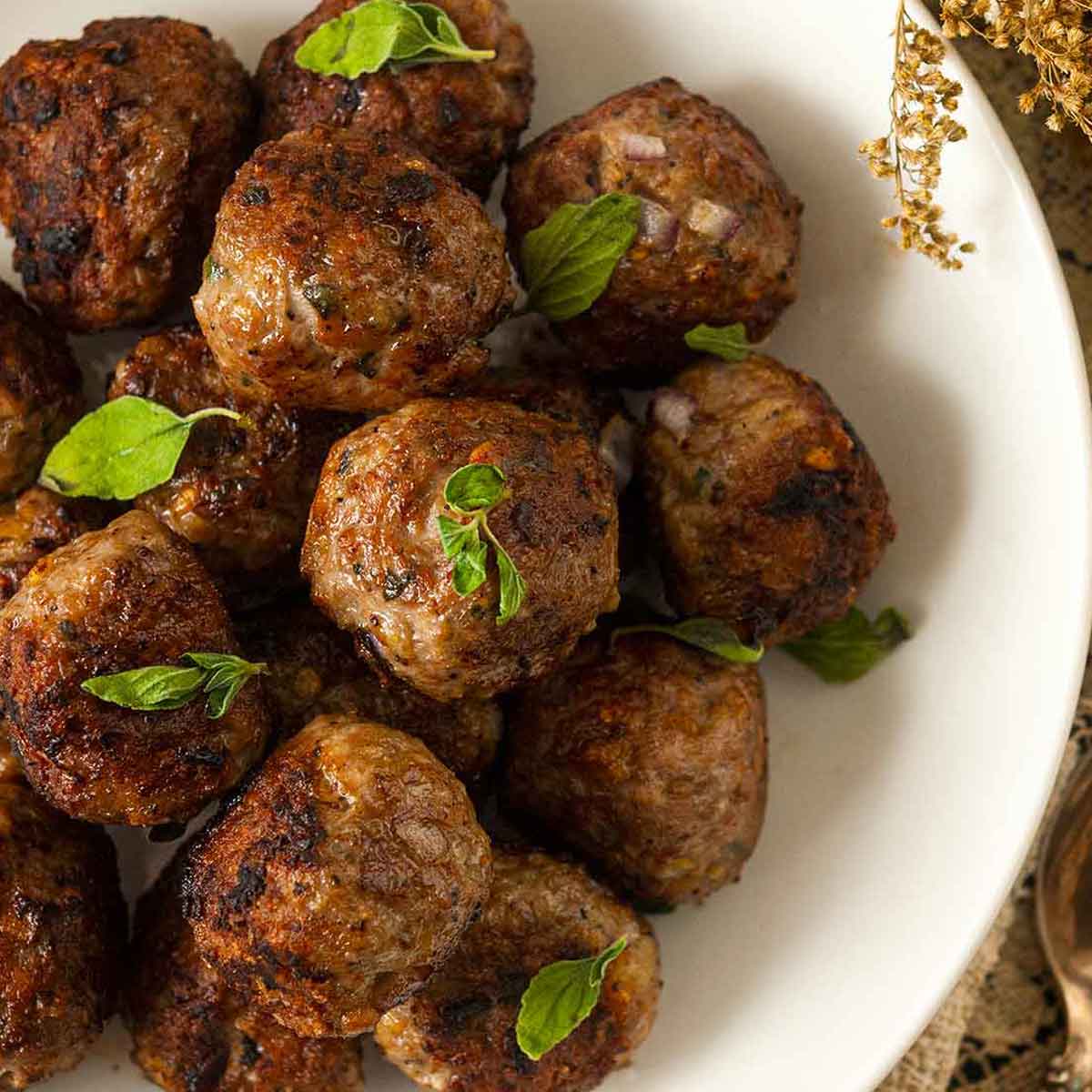 About 15 meatballs in a bowl, sprinkled with fresh oregano.