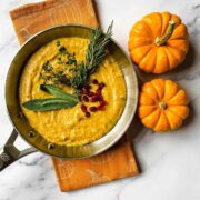 A pan of pumpkin cream sauce on a table beside 2 small pumpkins.