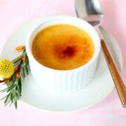 A creme brûlée on a saucer with flowers and a spoon.