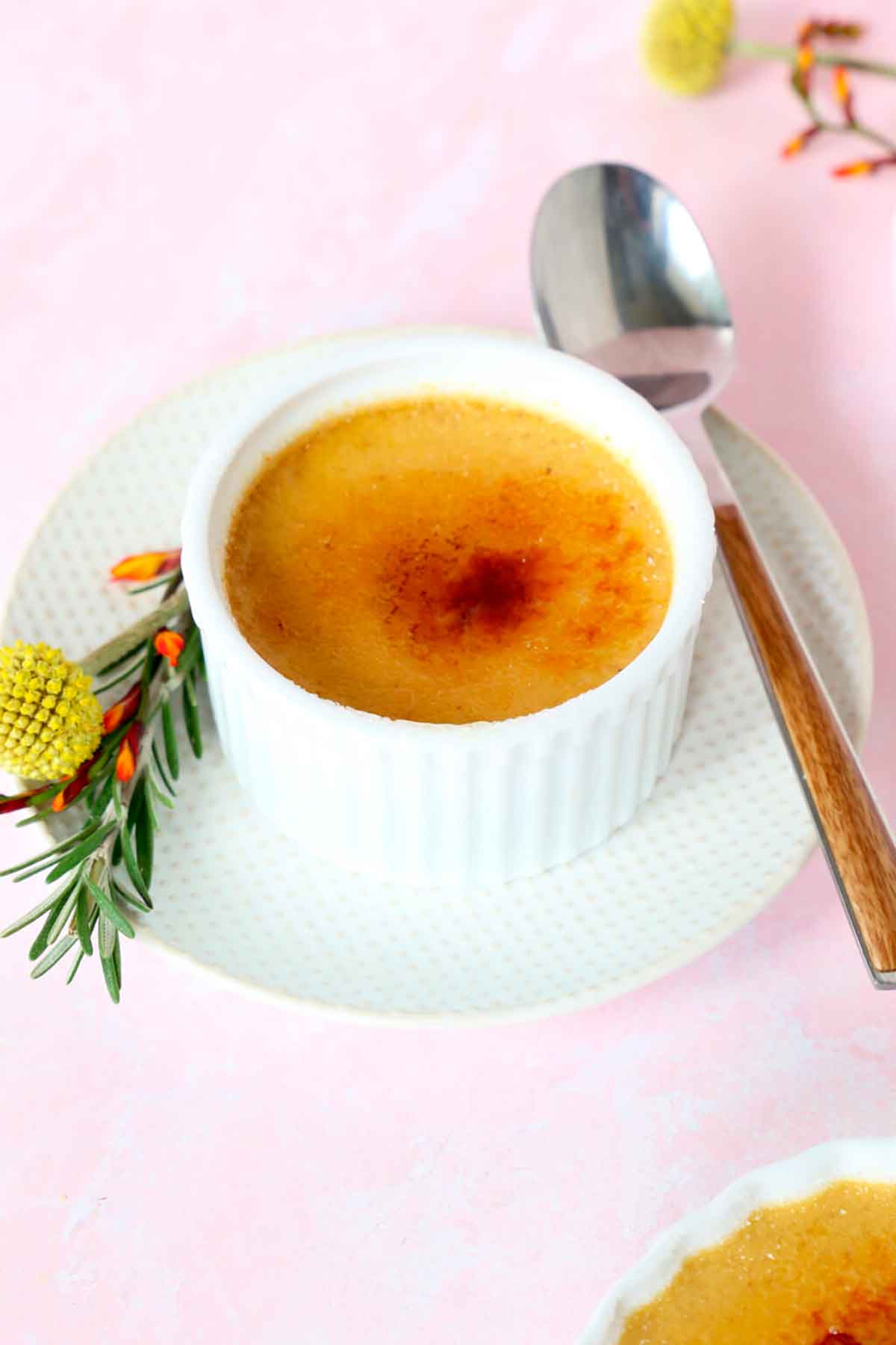 A creme brûlée on a saucer with flowers and a spoon.