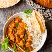 Pumpkin curry in a bowl with rice and bread on a table.