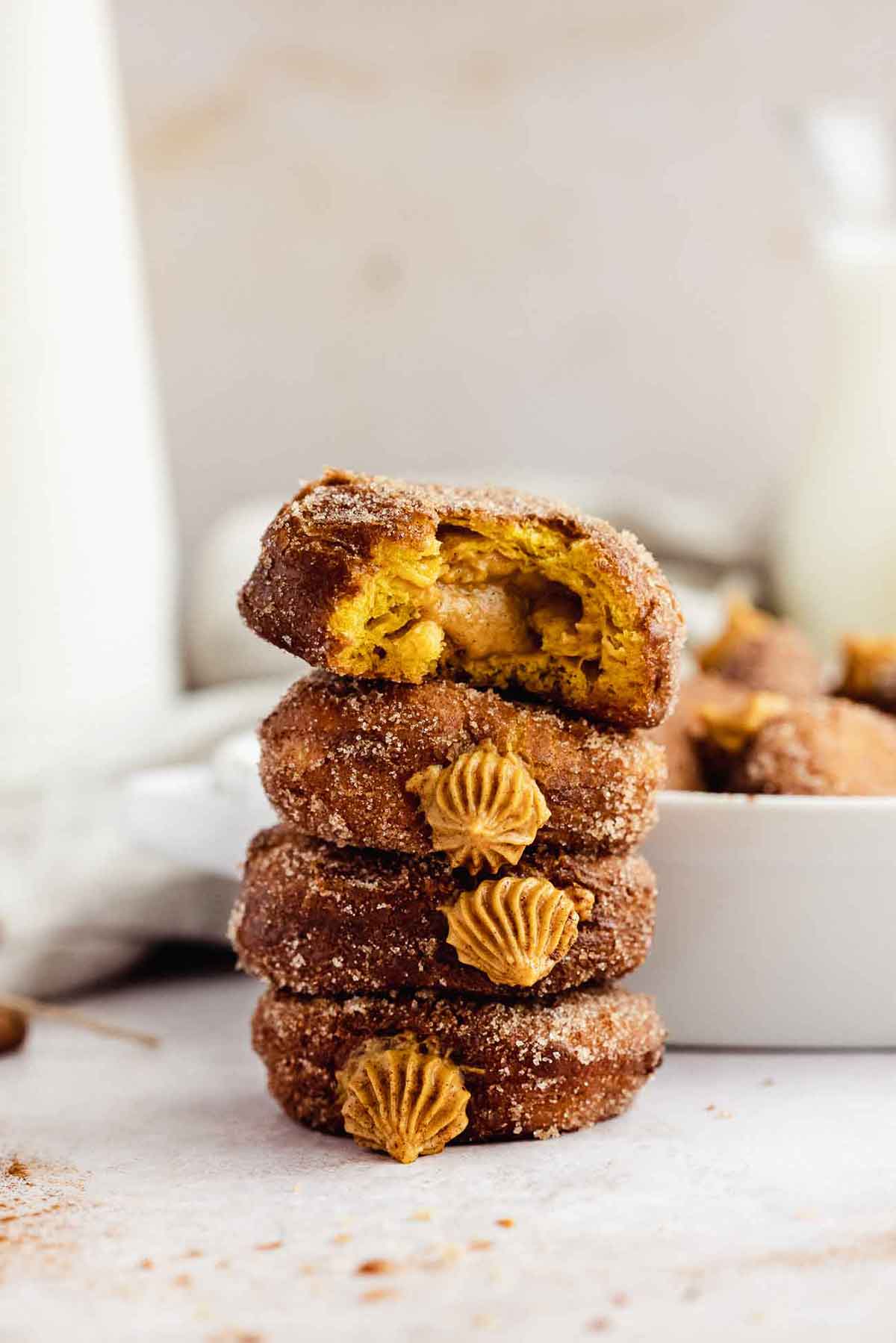 4 stacked pumpkin doughnuts with cream filling exposed on a table.
