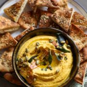 Pumpkin hummus in a bowl, on a plate with small pieces of bread.