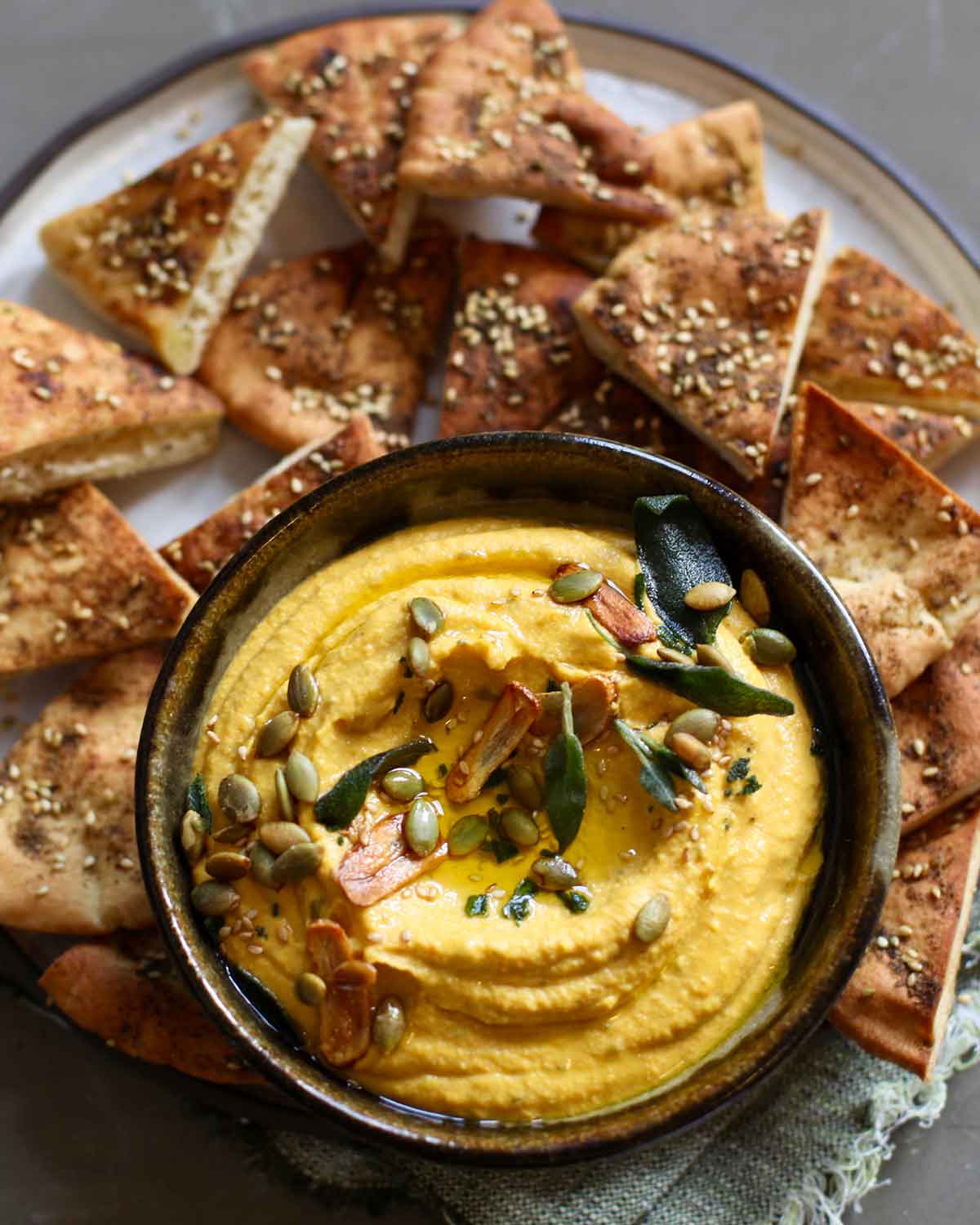 Pumpkin hummus in a bowl, on a plate with small pieces of bread.