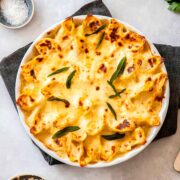 A round dish of baked pasta on a table, garnished with leaves.