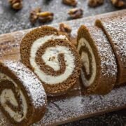A sliced pumpkin roll on a wooden board, sprinkled with sugar.