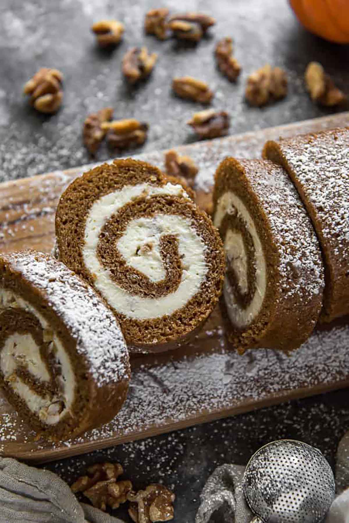 A sliced pumpkin roll on a wooden board, sprinkled with sugar.