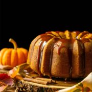 A pumpkin cake on a wooden table beside a small pumpkin and scattered pinecones.