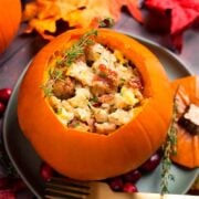 A pumpkin filled with stuffing on a plate, surrounded by autumn leaves.