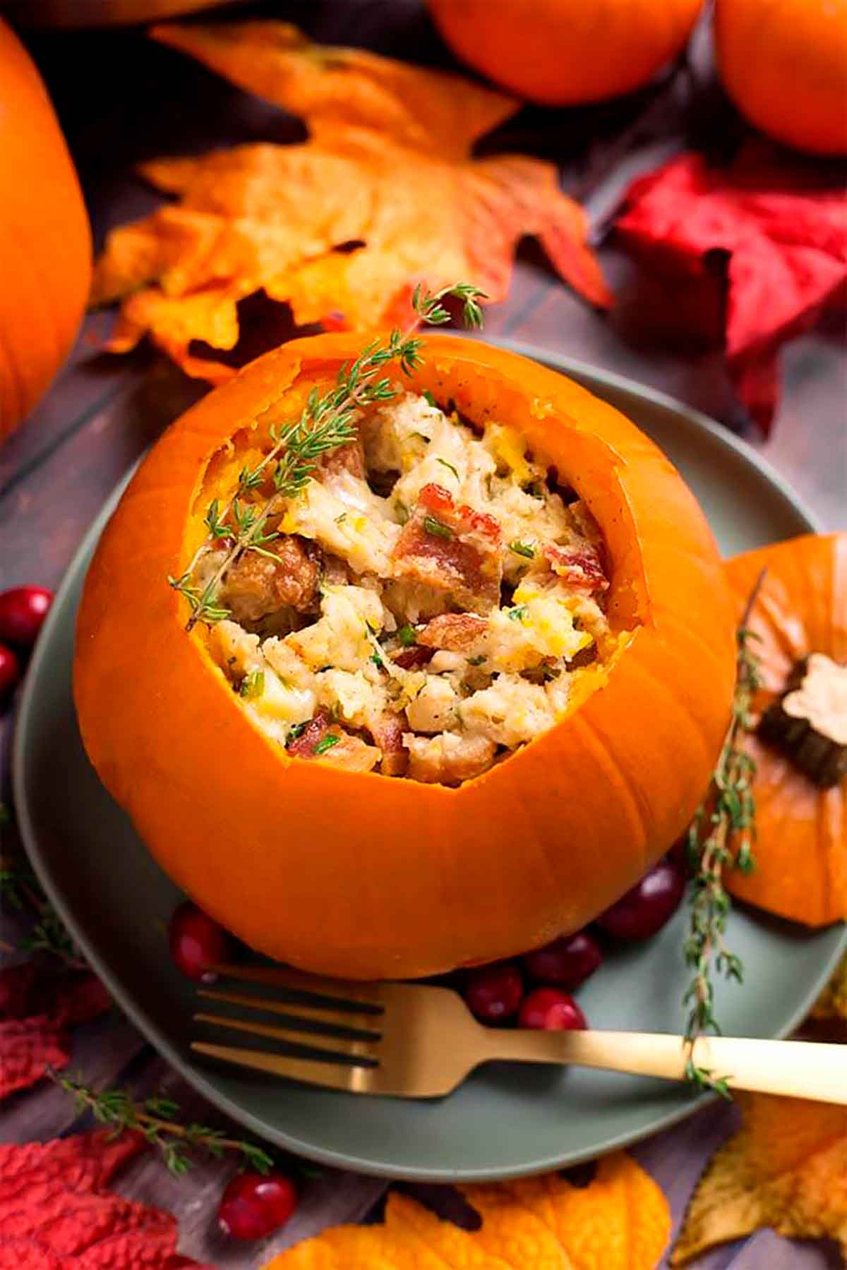 A pumpkin filled with stuffing on a plate, surrounded by autumn leaves.