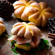 A small sandwich topped with a pumpkin roll on a table, with 2 pumpkin rolls in the background.