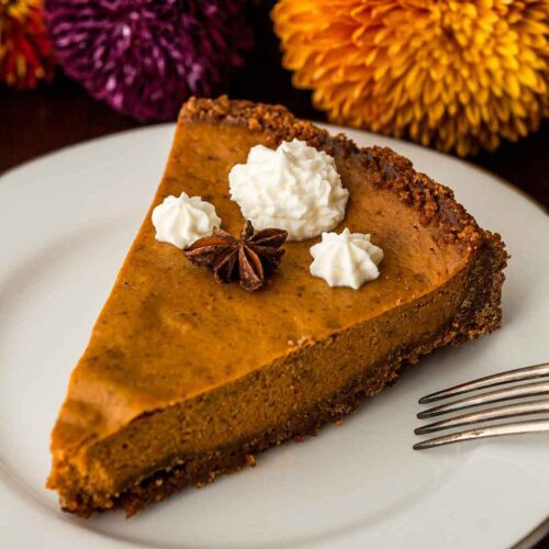 A slice of masala chai pumpkin pie topped with whipped cream and star anise beside flowers.