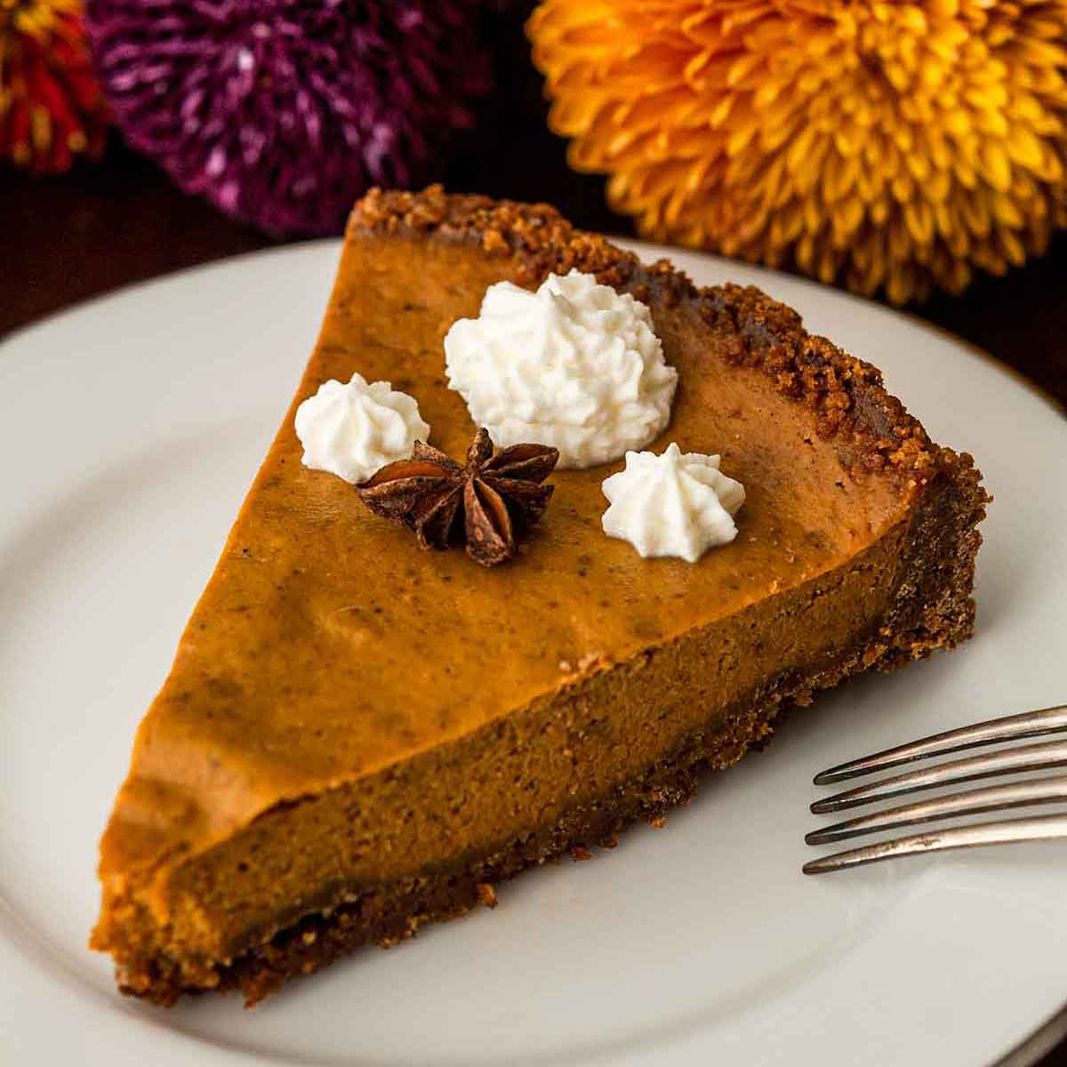 A slice of masala chai pumpkin pie topped with whipped cream and star anise beside flowers.