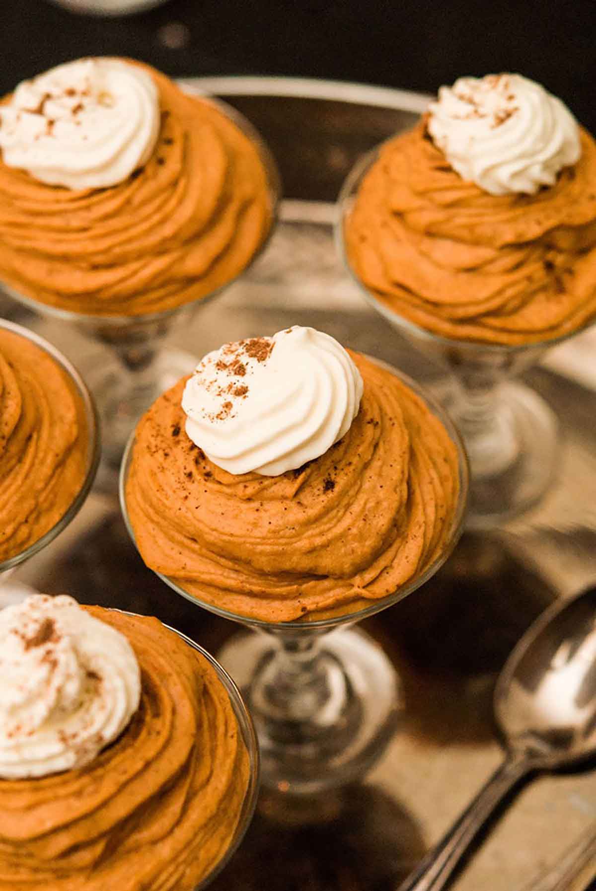 5 small glasses full of pumpkin mousse topped with whipped cream, sitting on a silver tray.