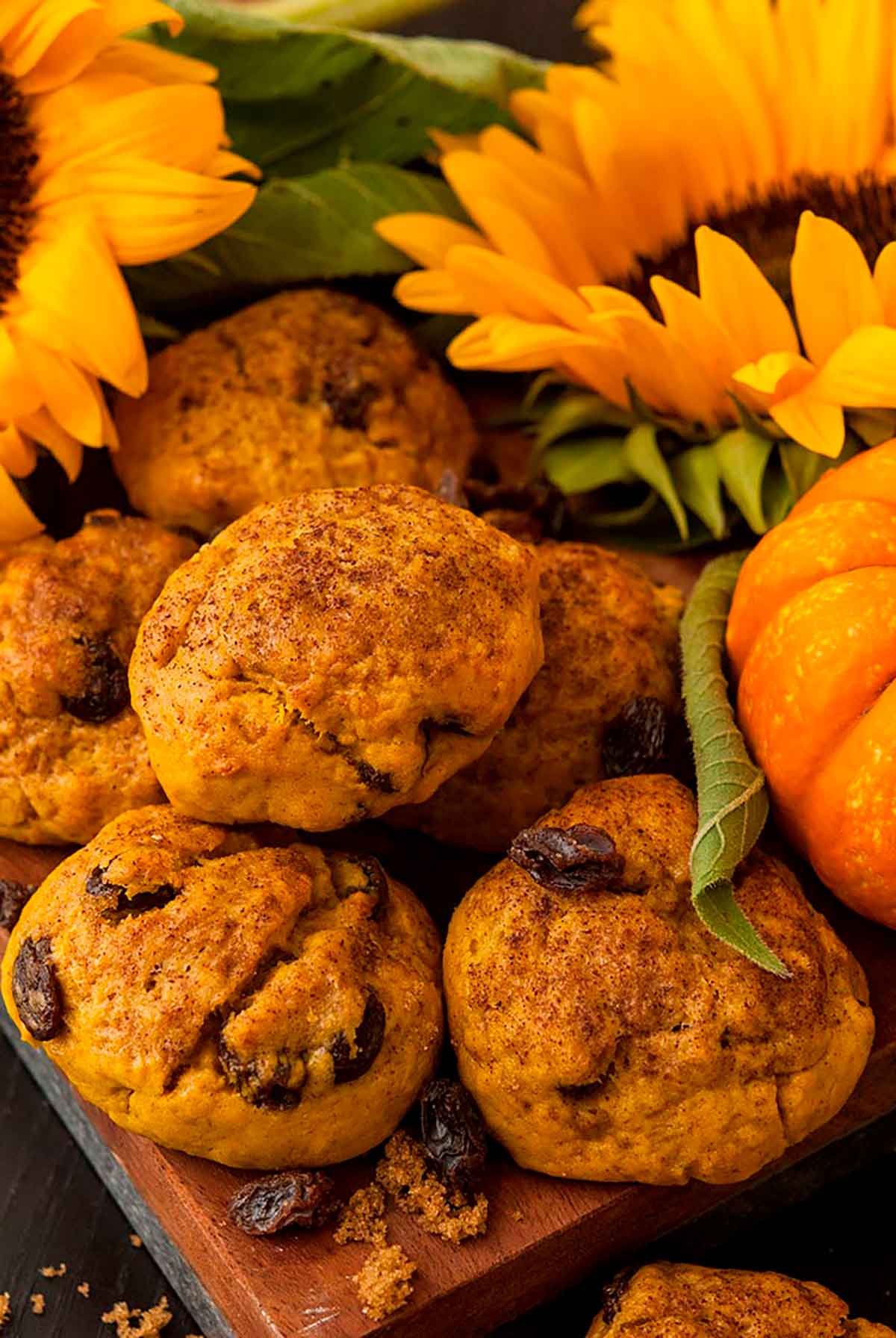 Pumpkin scones beside a small pumpkin and sunflower on a wooden board.