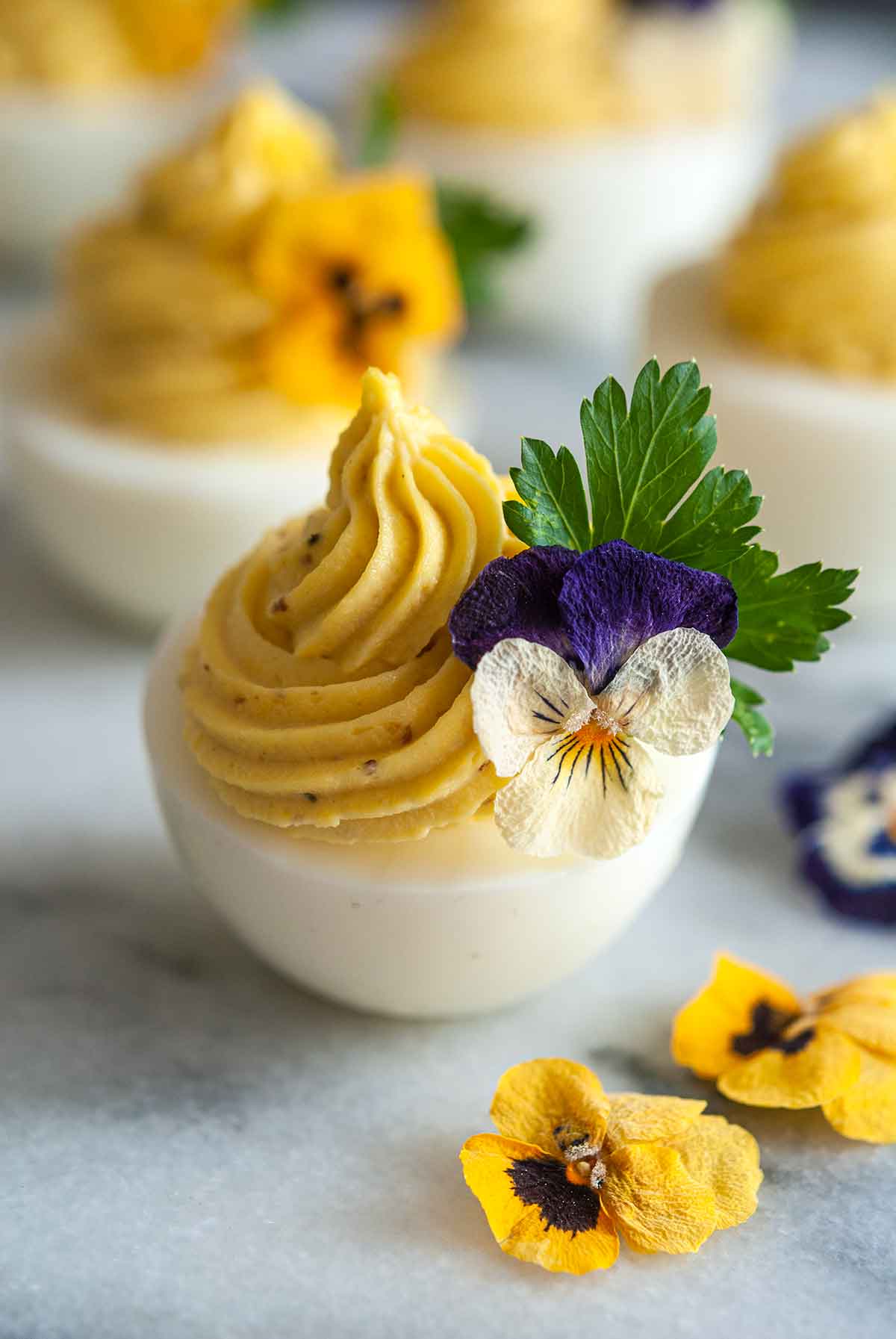 5 deviled eggs, garnished with flowers on marble.