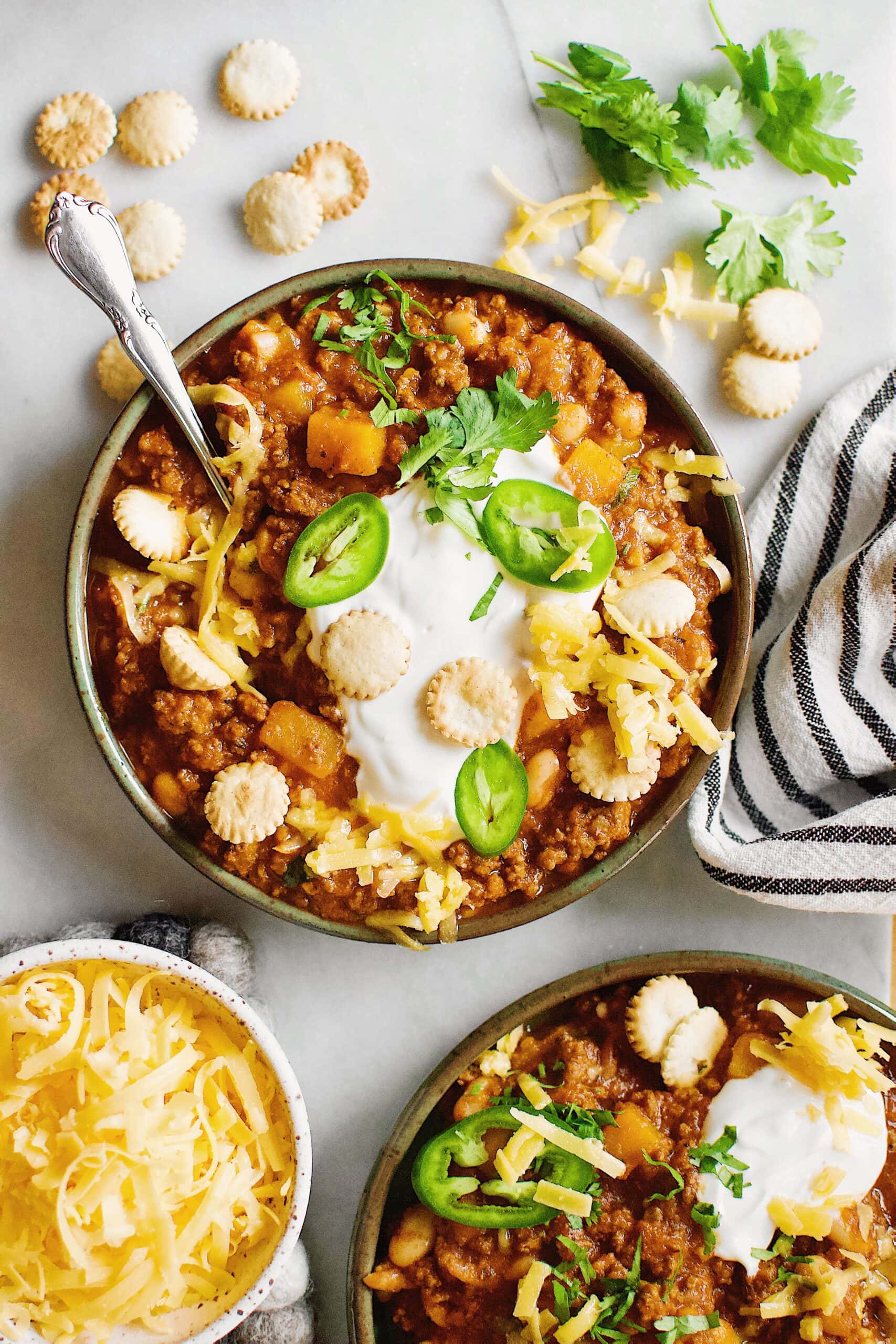 2 bowls of pumpkin chili on a table, garnished with cream, cheese and jalapeno.