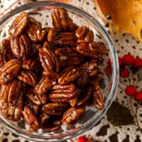 A bowl of candied pecans on a lace table cloth, surrounded by fall leaves.