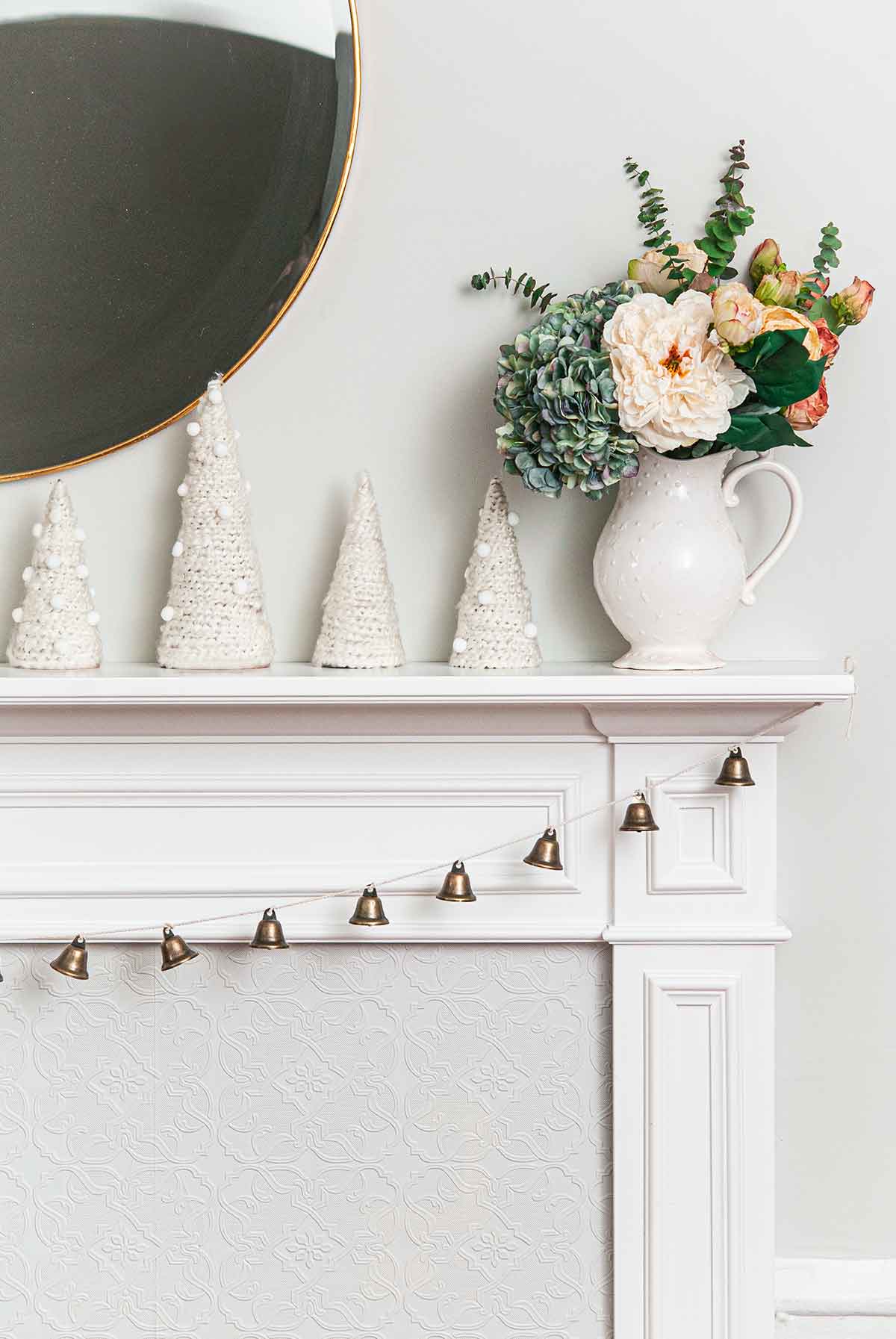 A mantle with a string of bells, yarn trees and a floral bouquet.