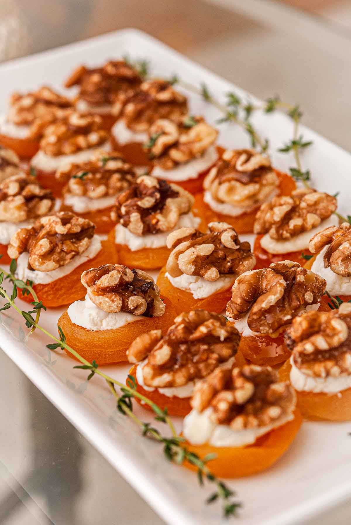 About 20 apricot appetizers on a plate, garnished with thyme.