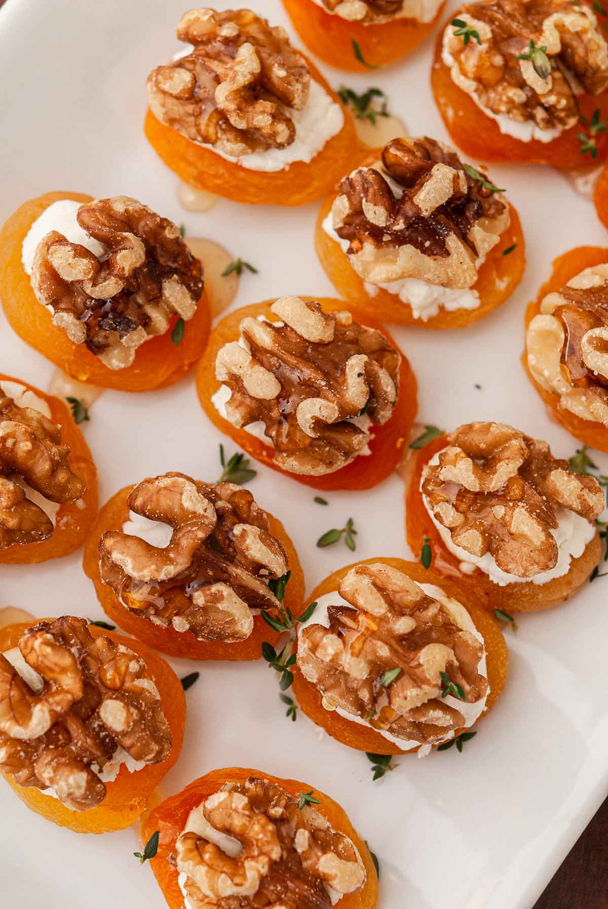 About 12 apricot appetizers on a plate, sprinkled with thyme.