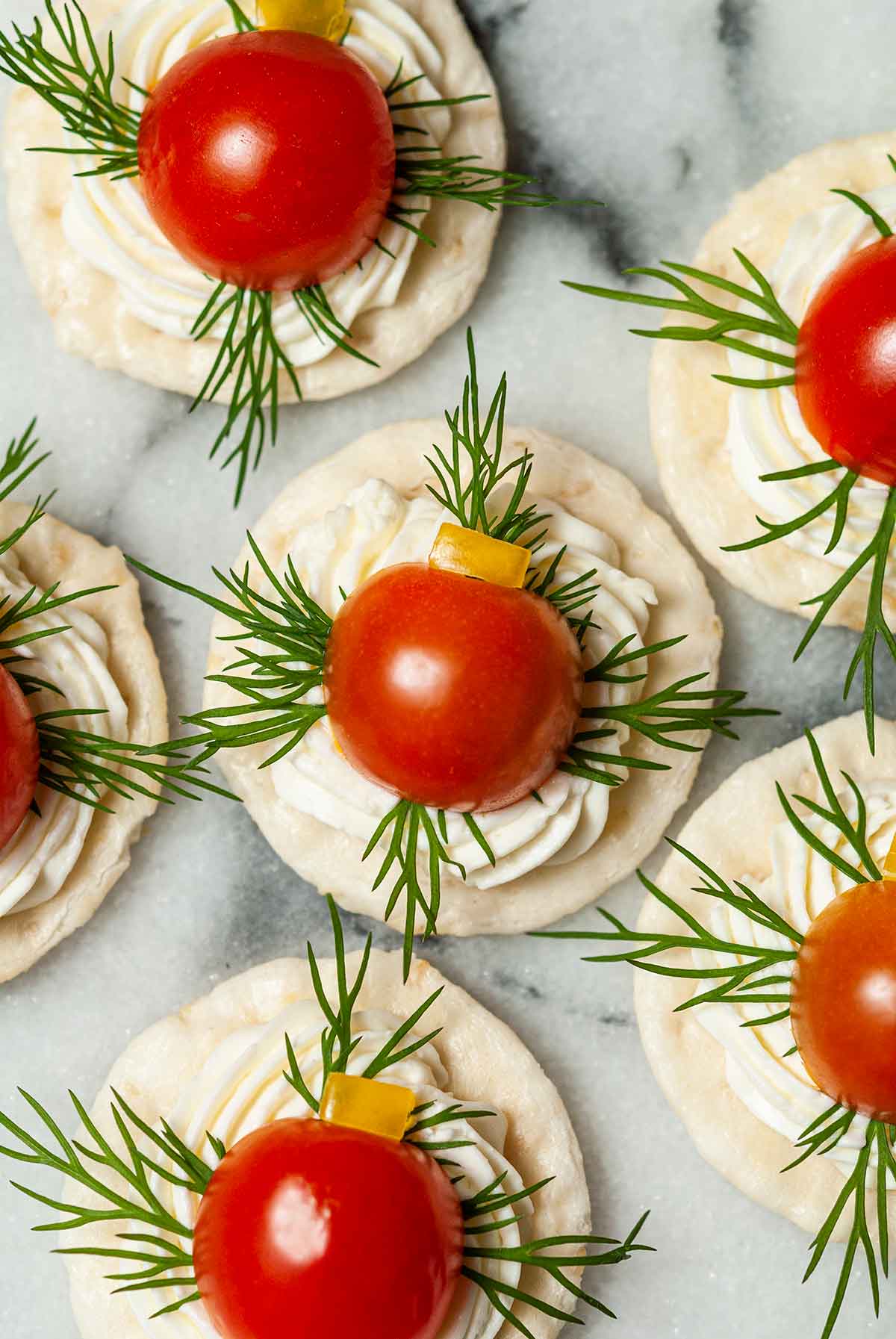 6 appetizers with cheese, dill, tomato and pepper on a cracker on marble.