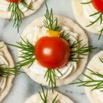 An appetizer with cheese, dill, tomato and pepper on a cracker on marble.