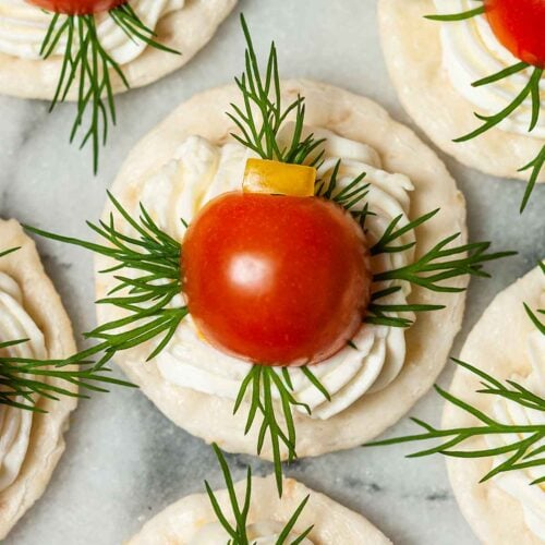 An appetizer with cheese, dill, tomato and pepper on a cracker on marble.