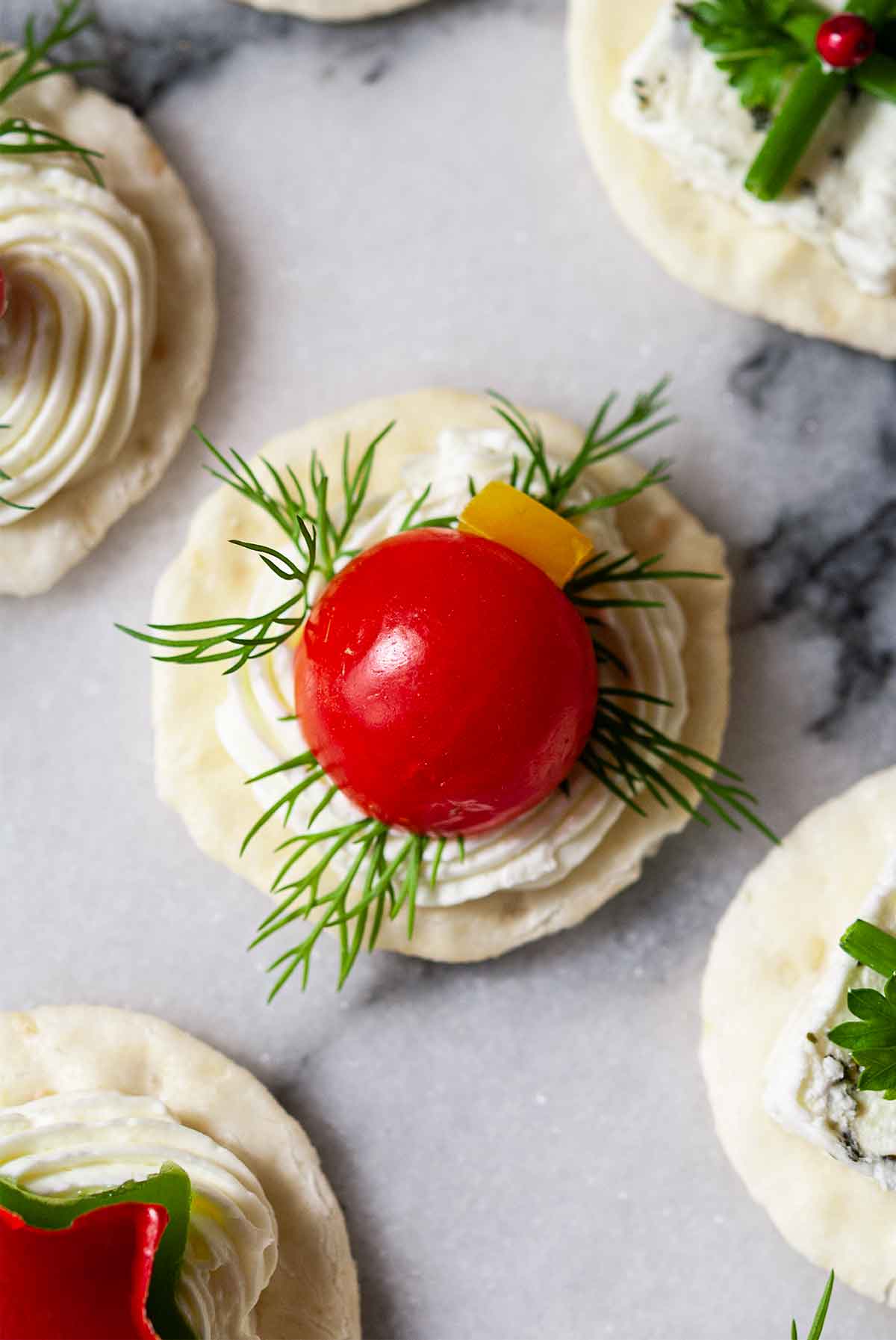 A Christmas ornament appetizer with tomato and dill on marble with 4 others.