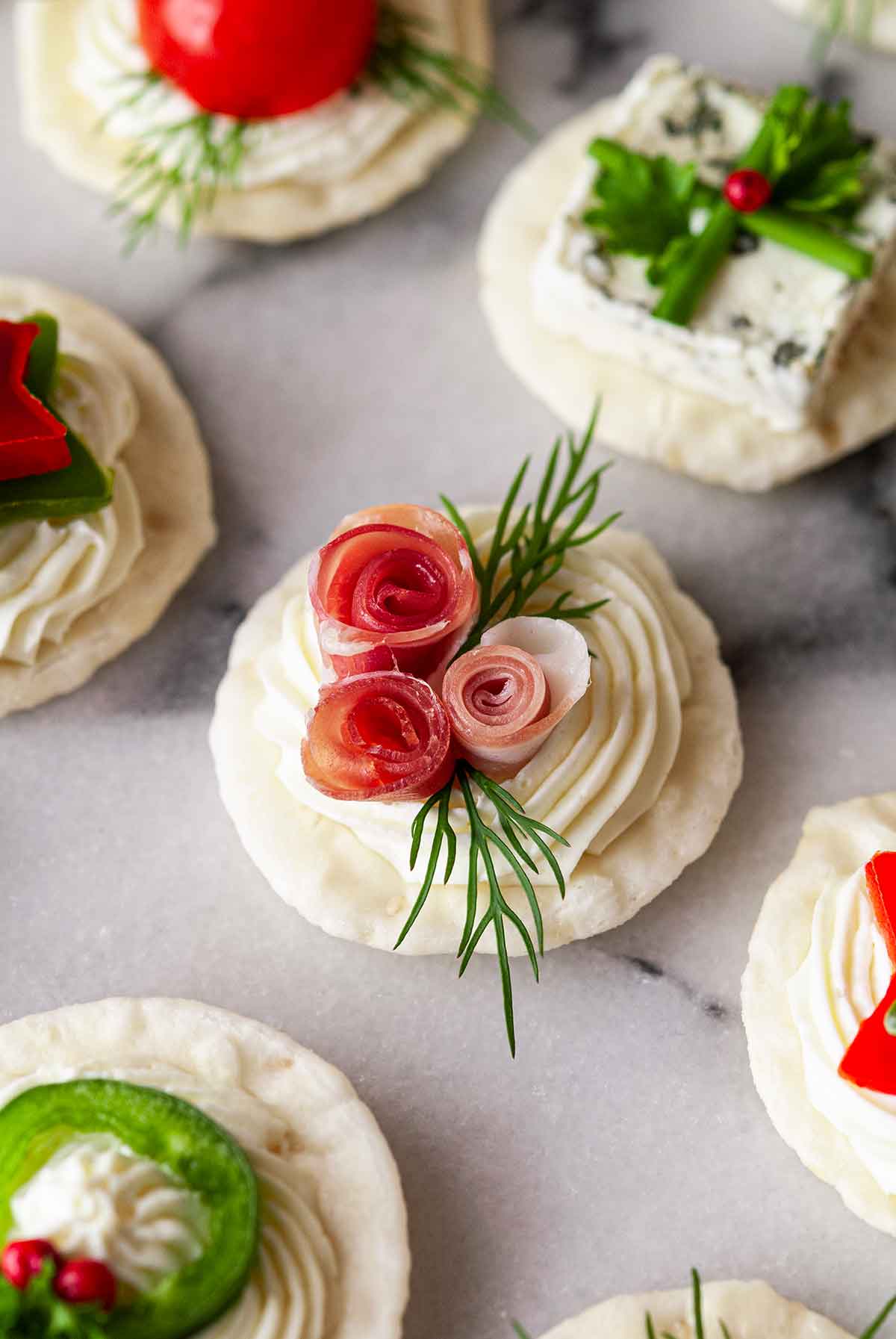 An appetizer with 3 prosciutto roses and dill beside 5 festive appetizers.