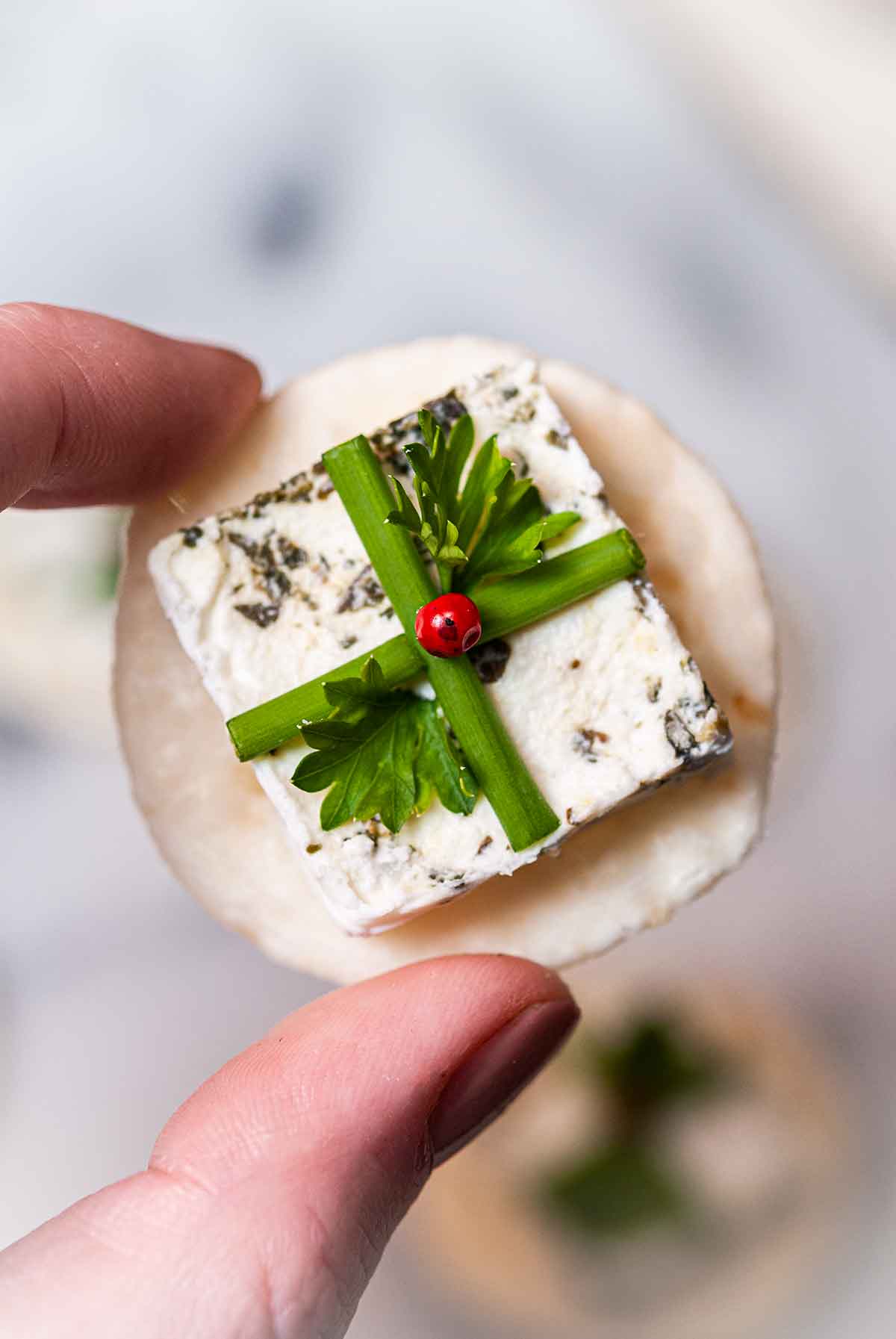 Fingers holding an appetizer that looks like a present on a cracker.
