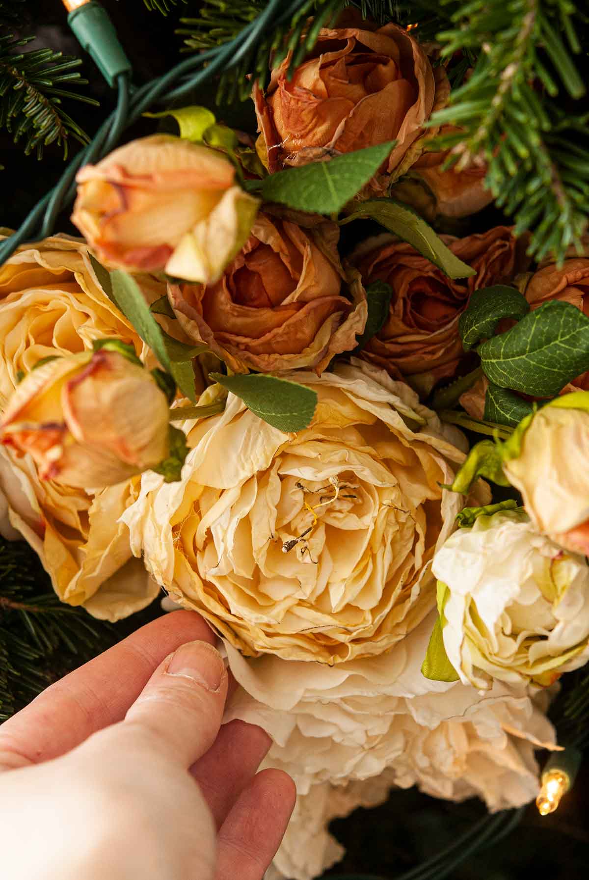 A hand positioning a bouquet of flowers in a Christmas tree.